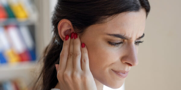 Woman holding her ear in pain due to TMJ disorder in New Jersey