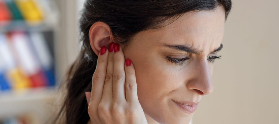 Woman holding her ear in pain due to TMJ disorder in New Jersey