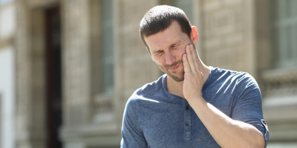 Man standing in front of a building and clutching his jaw in pain from clicking and popping.