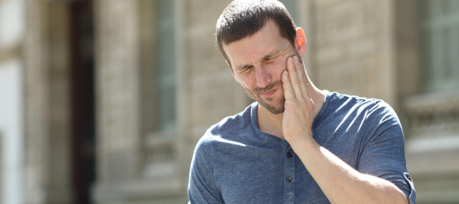 Man standing in front of a building and clutching his jaw in pain from clicking and popping.