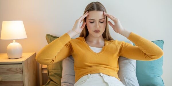 Young woman sitting in her bed and clutching her head in pain from overnight jaw clenching.